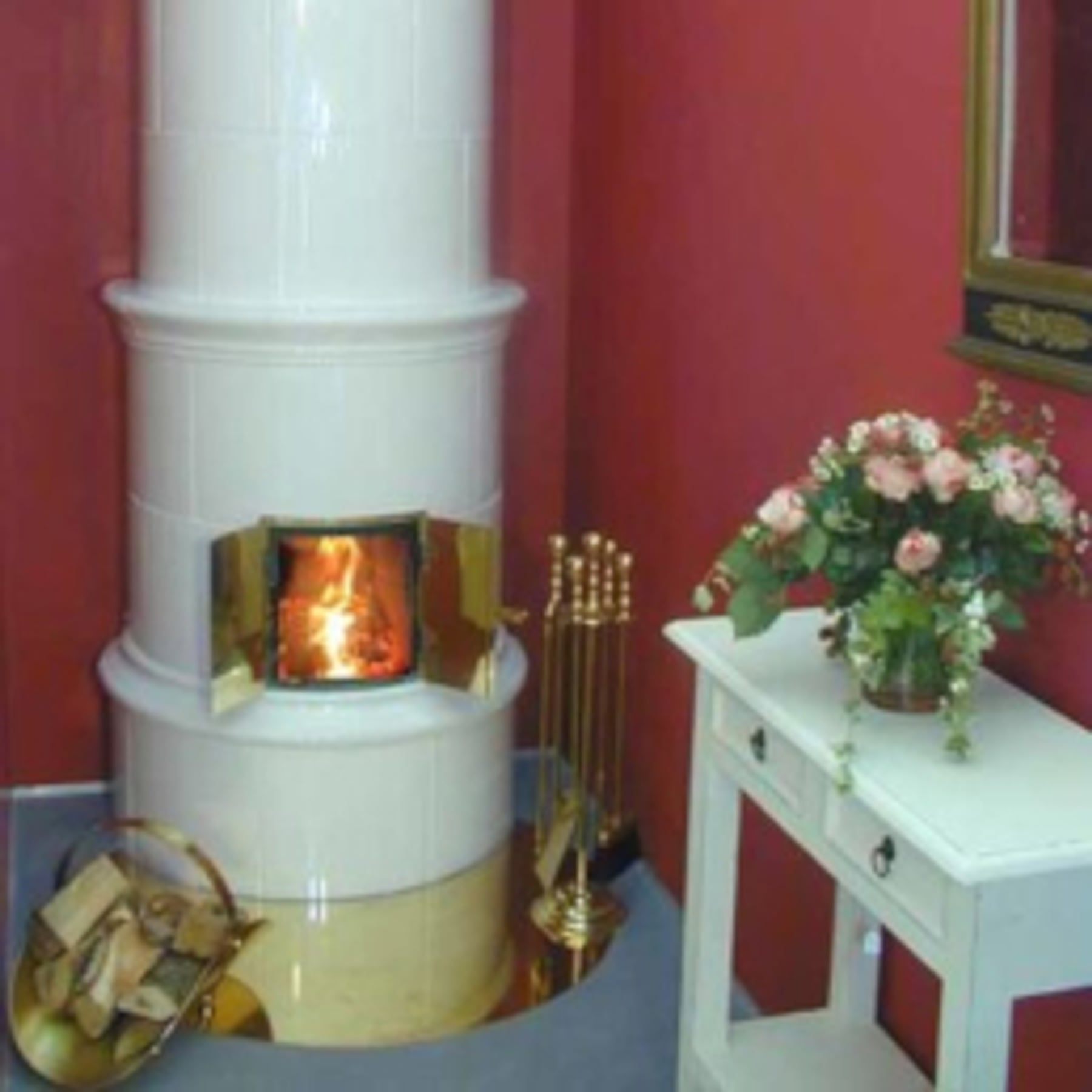 Weißer Kachelofen mit Messingdetails und offenem Feuer